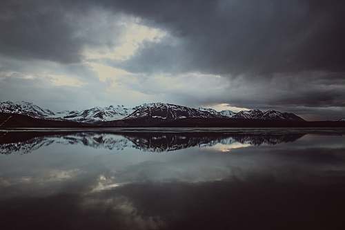 grey landscape photo of body of water with mountain covered with snow paxson lake